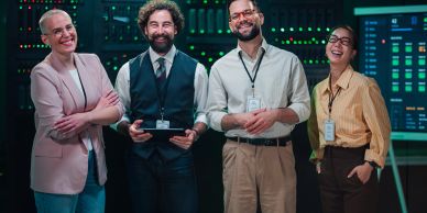 Four colleagues smiling in a tech workspace.