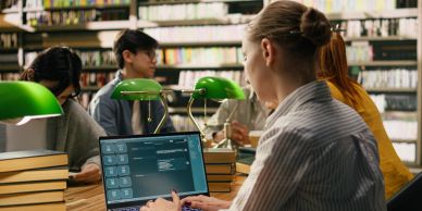 Person working on a laptop in a library with others in background.