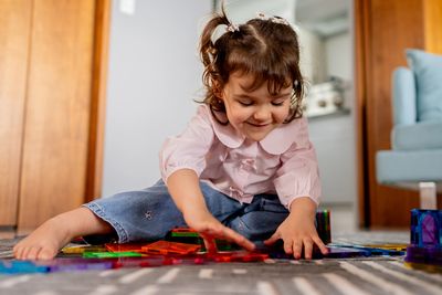 Little girl playing with colorful tiles on floor.