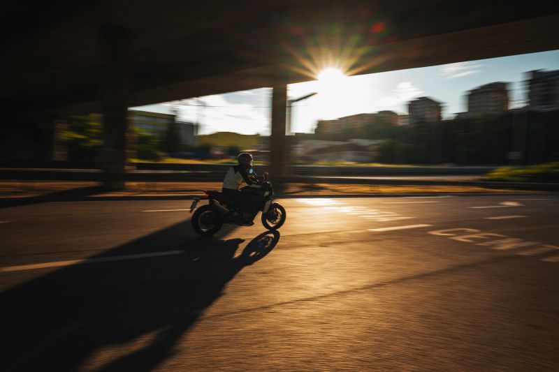 Motorcyclist riding through urban streets at sunset with dynamic motion blur. Golden hour light, transportation, commuting, speed, and modern city lifestyle.