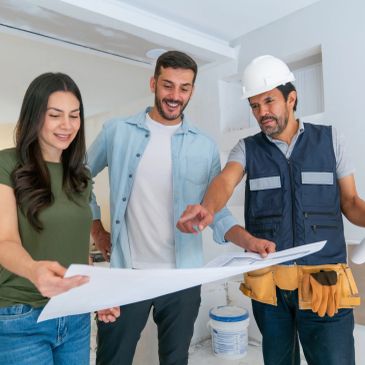 Three people reviewing construction plans indoors.