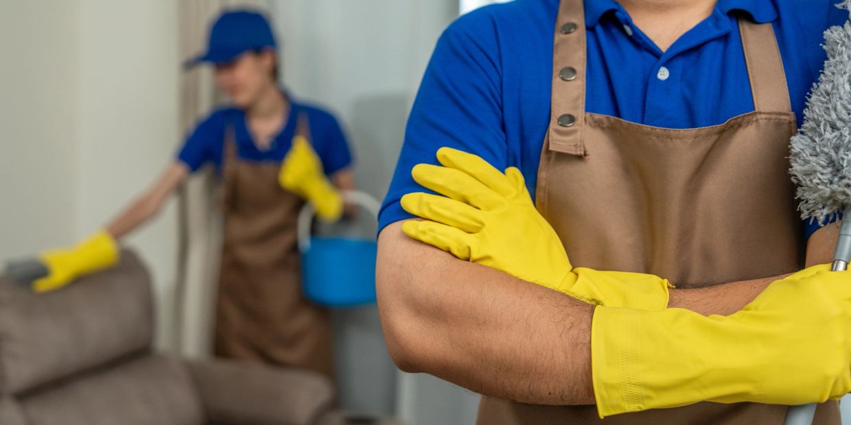 Two cleaners in blue uniforms and yellow gloves working indoors.