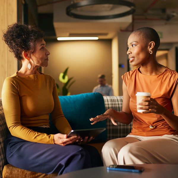 Two women having a conversation while sitting on a sofa.