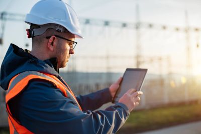 Engineer in safety gear using a tablet outdoors.