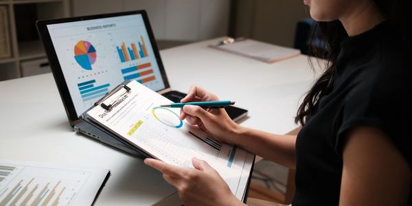Person analyzing business data on clipboard and laptop.