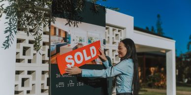 Woman placing a sold sign on a real estate board.