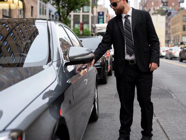 A chauffeur holding open the door of a black luxury car.