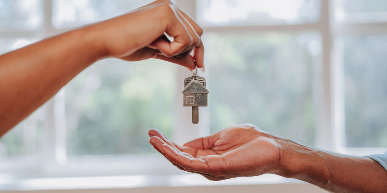 Person handing over house key to another.