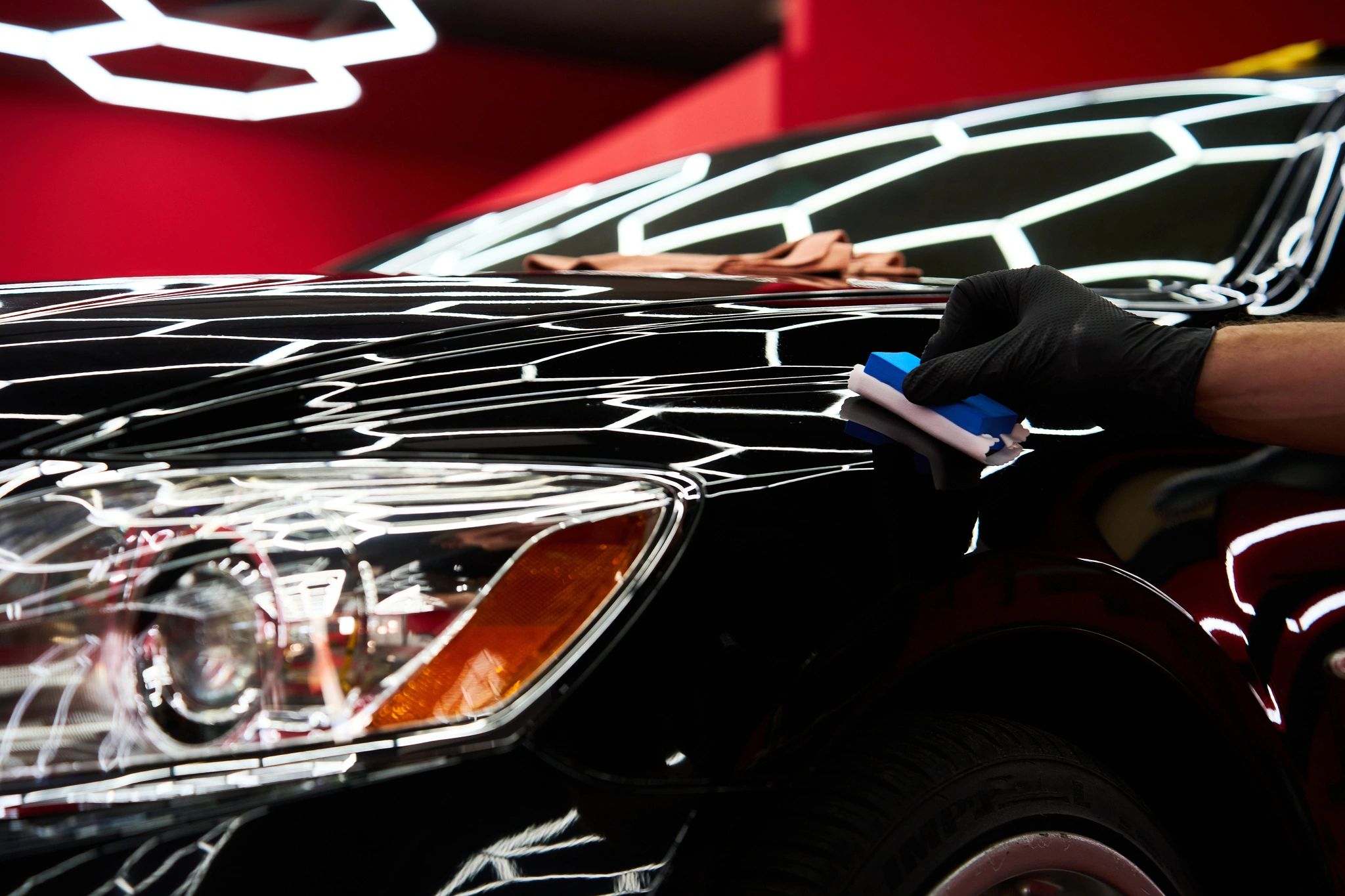 Hand polishing a black car's hood with bright lights.
