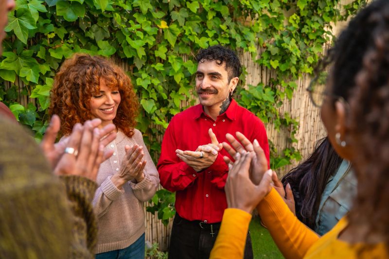 Diverse group of adults in an outdoor support circle, smiling, clapping and showing empathy during a mental health discussion, celebrating recovery, connection and hope