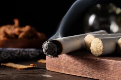 Burning cigarette with ash on a wooden surface.