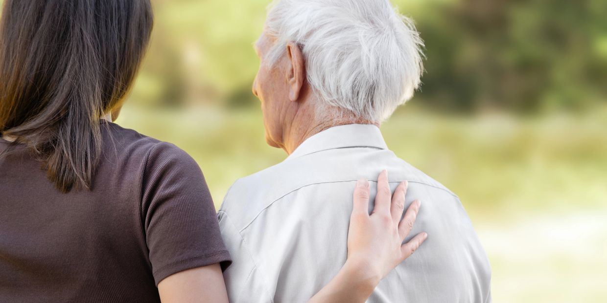 Elderly man looking out and a young woman has her hand on his back.