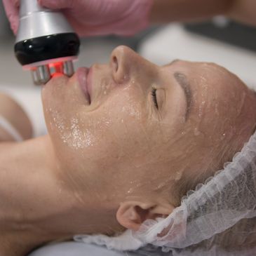 Woman receiving facial treatment with a handheld device.