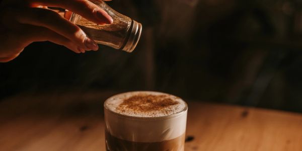 Sprinkling cinnamon on a frothy coffee.