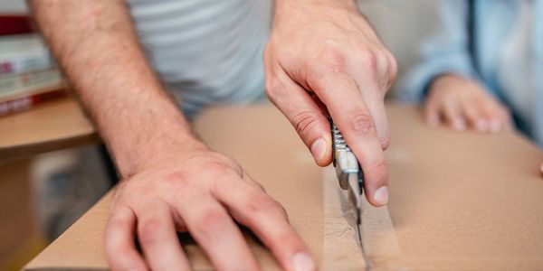 Hands cutting cardboard with a utility knife.