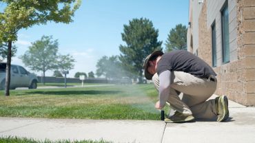  adjusting a sprinkler on grass near a building.