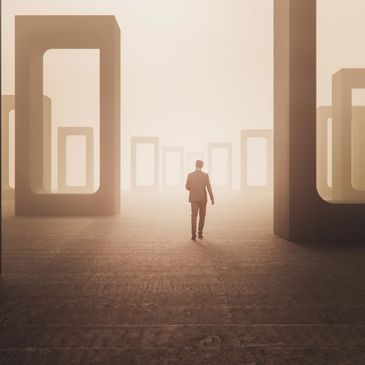 Man walking amid giant rectangular stone arches in foggy environment.