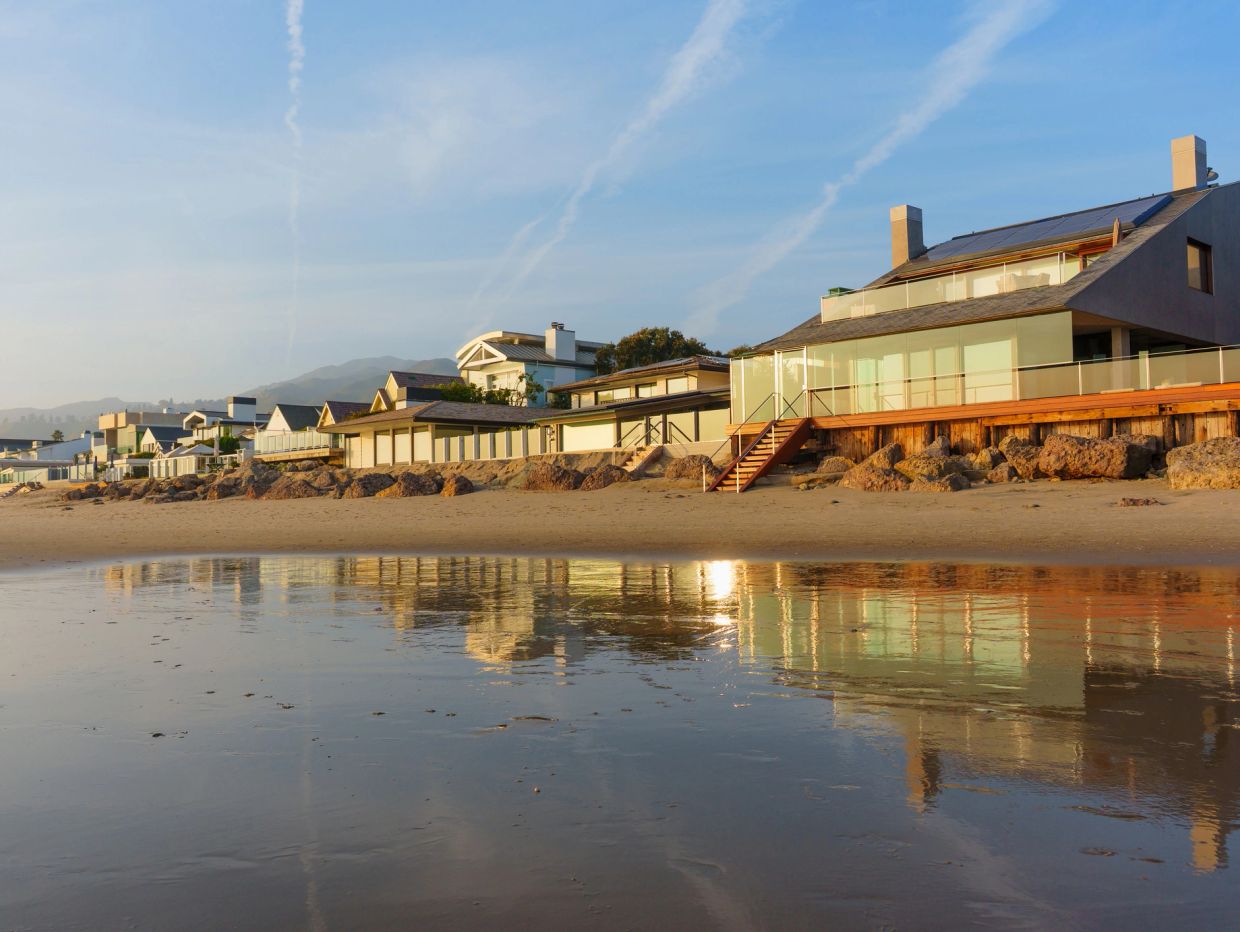Beachfront houses with glass balconies reflecting on wet sand.