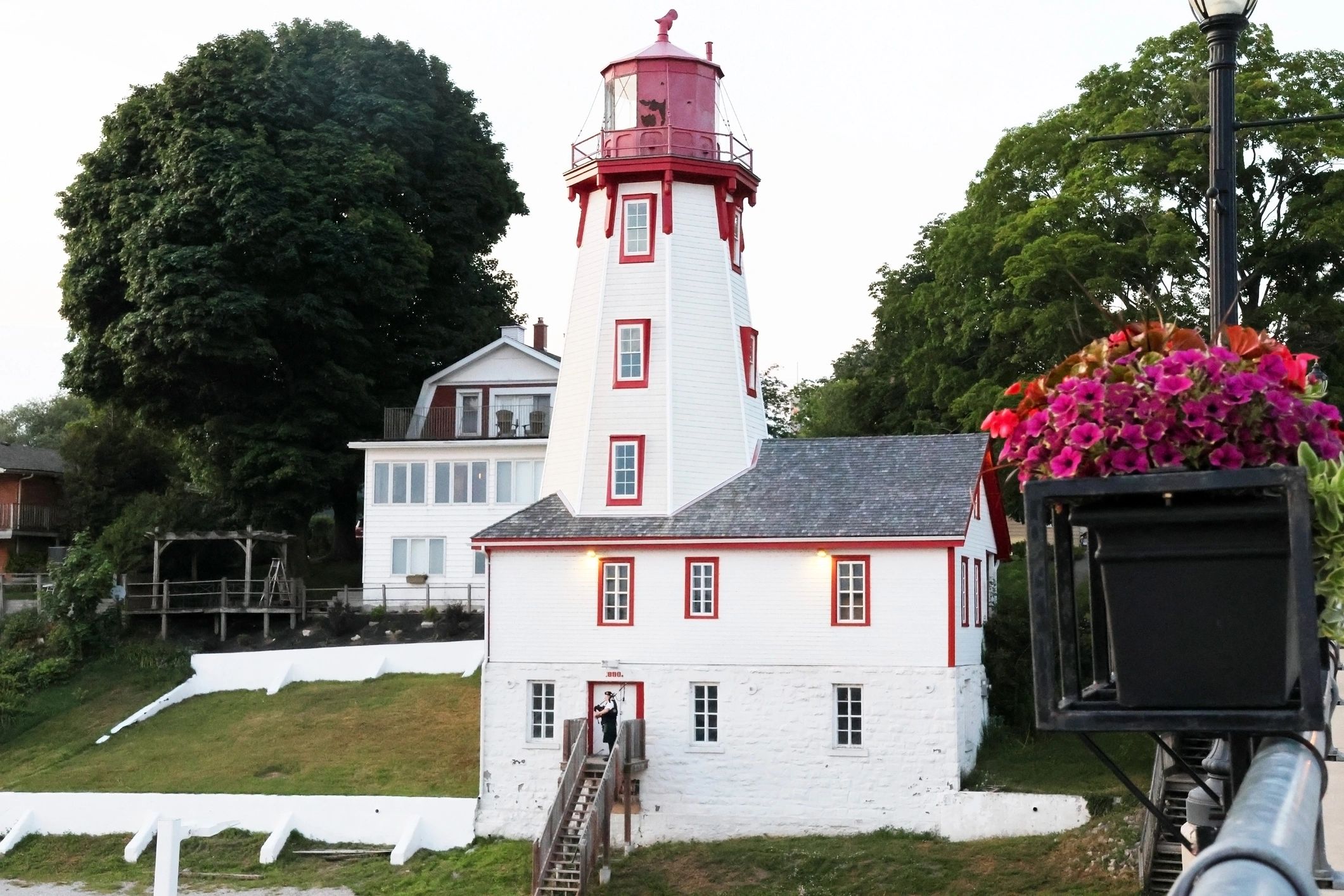White building with red lighthouse tower surrounded by trees and flowers.