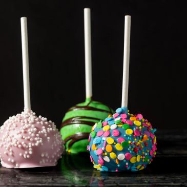 Three colorful sprinkled cake pops with sticks.
