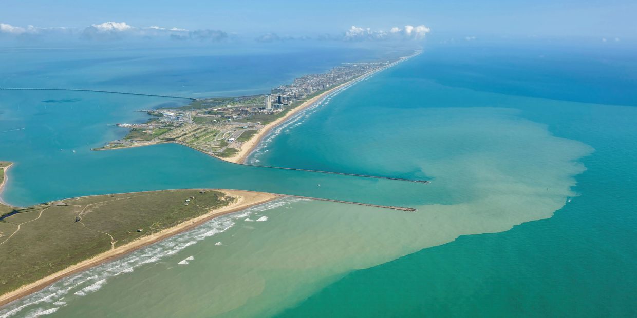 A narrow peninsula stretching into the ocean under a blue sky.