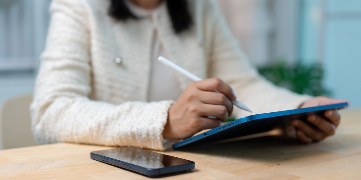 Person using stylus on tablet, phone on table.
