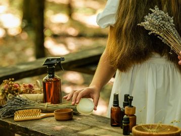 Woman holding dried lavender behind her back with skincare items on table.