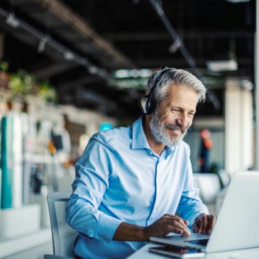 Homme souriant avec casque travaillant sur un ordinateur portable.
