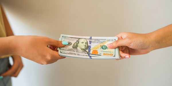 Person handing over a stack of US dollar bills to another.