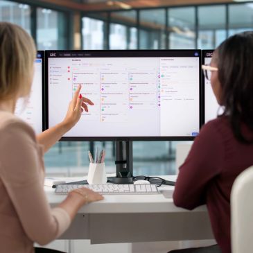 Two women collaborating at a computer with a task management app open.