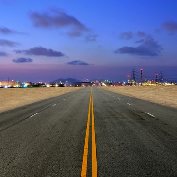 Empty road leading towards an industrial area at dusk.