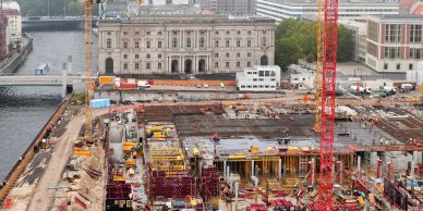 Large construction site near a river and city buildings.