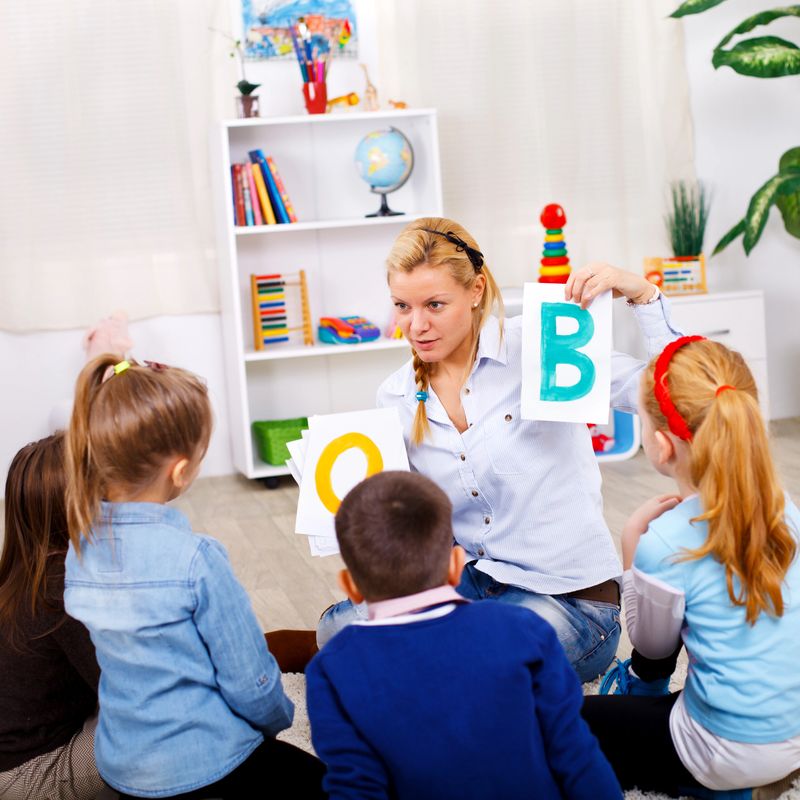 Teacher is teaching letters to preschoolers while sitting on the floor