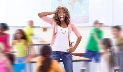 Excited teacher in classroom with blurred students moving around.