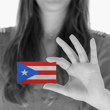A woman holding a small Puerto Rican flag with a black and white background.