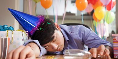 Man asleep at a party with balloons, gifts, and confetti around.