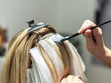 Person applying hair dye with brush and foils for highlights.