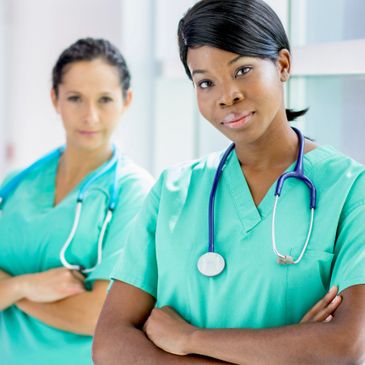 Two confident female healthcare professionals in scrubs with stethoscopes.