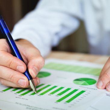 Person analyzing green bar and pie charts with a pen.