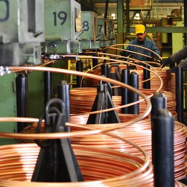 Workers in a factory handling large coils of copper wire.