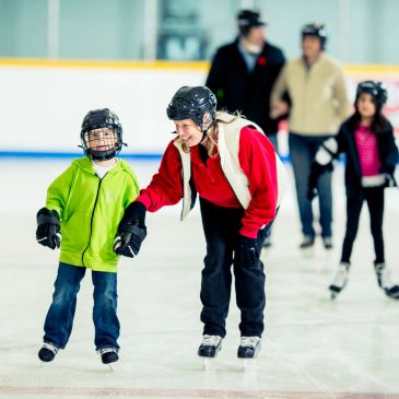People ice skating in an indoor rink, including a child and adults.