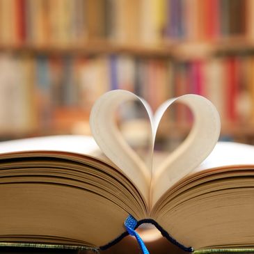 Pages of a book folded into a heart shape with a blurred bookshelf background.
