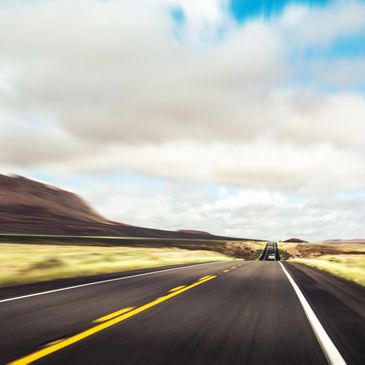 Open road stretching through a desert landscape under a cloudy sky.