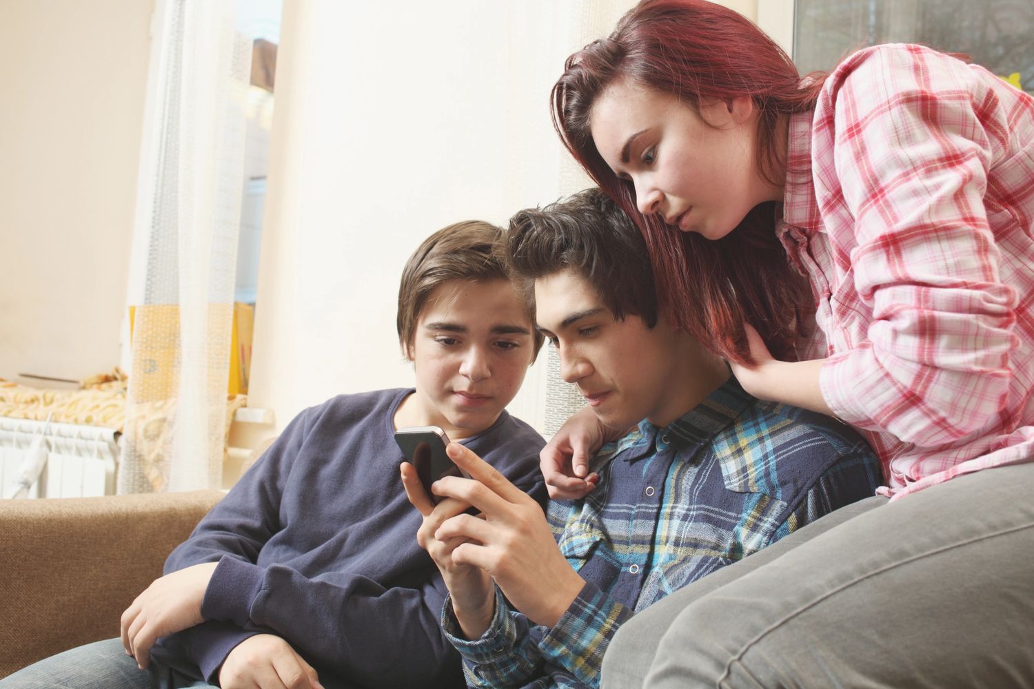 Three teenagers closely looking at a smartphone together indoors.