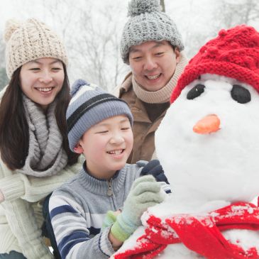Family building a snowman together on a winter day.