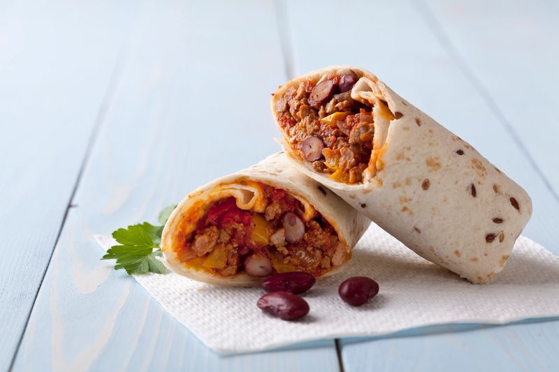 burritos wraps with meat beans and vegetables on blue wood board