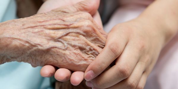 A young hand gently holding an elderly hand in a comforting gesture.