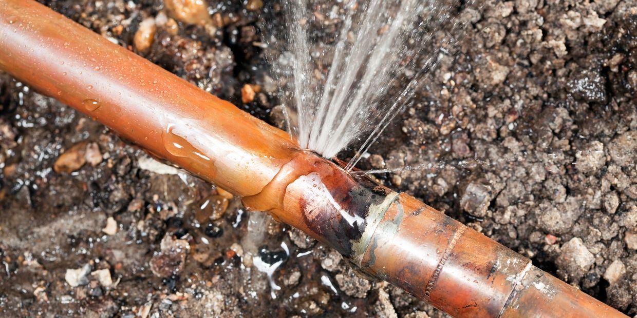 A copper pipe leaking water through a crack in the ground.