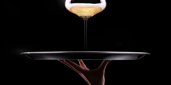 Hand holding a tray with a champagne glass glowing above it against a black background.