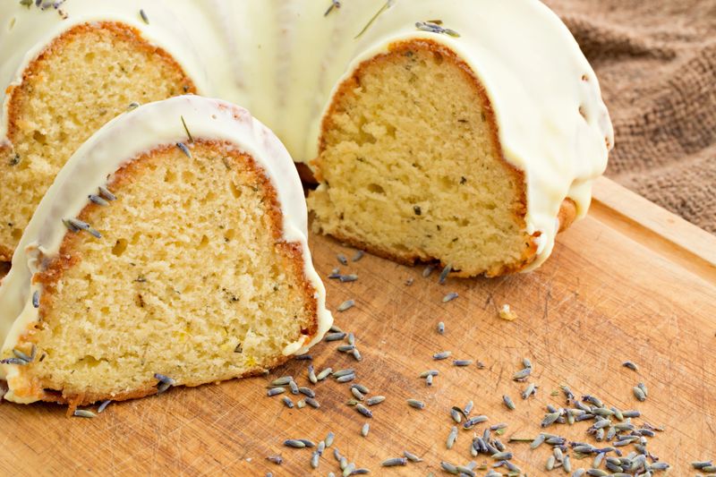 A close up shot of a lemon lavender bundt cake and some lavender blossoms on a wooden cutting board.